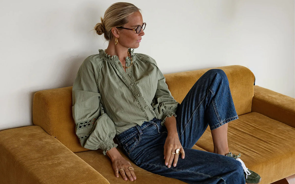 Woman in a green blouse and jeans relaxing on a mustard sofa